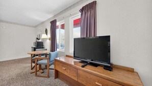 A hotel room with a TV on a wooden dresser, a desk with a lamp, and a chair. - Eagle Motel Suite 100 (Manitou Springs)