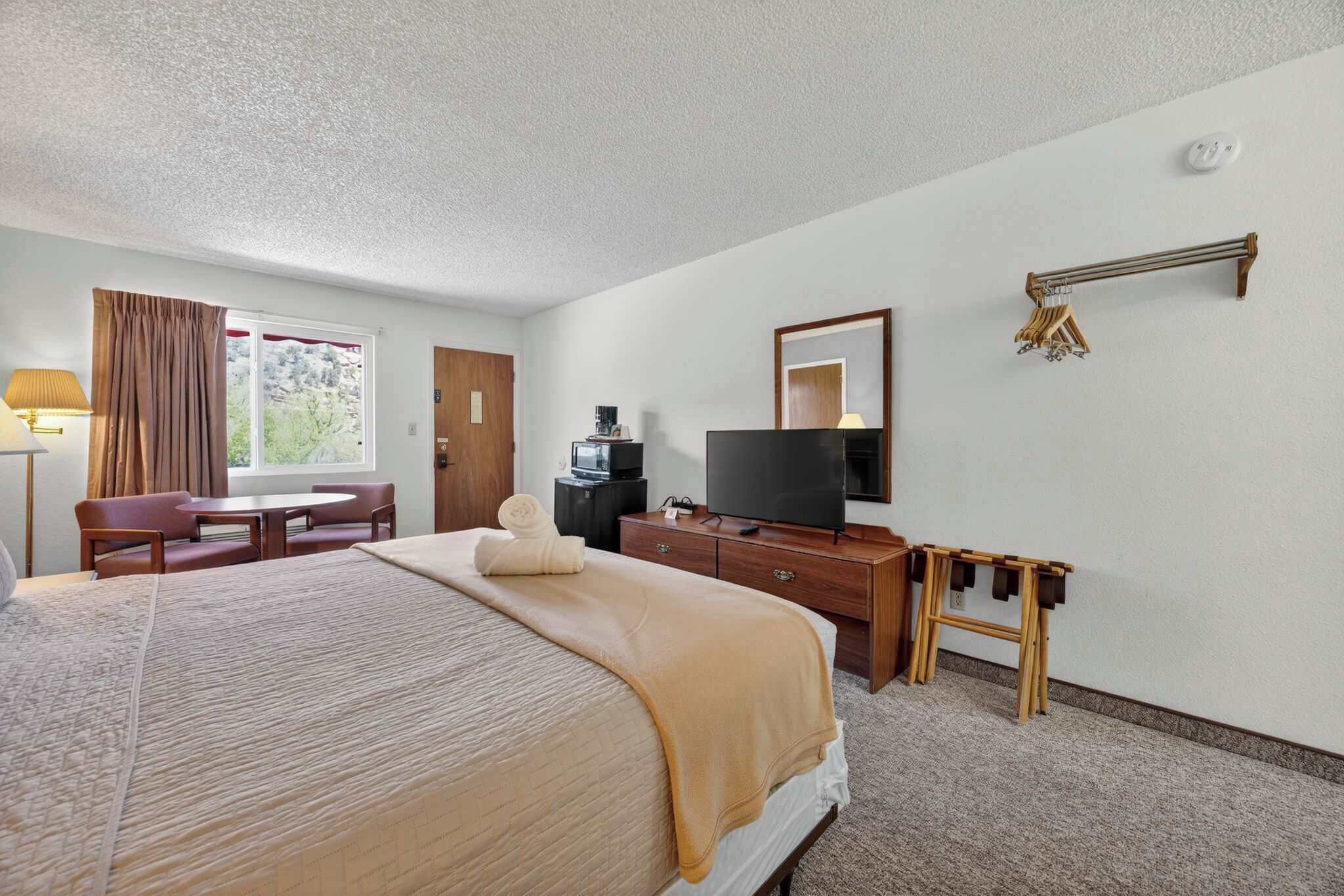 A hotel room with a bed, a desk, a television, a lamp, and a window with curtains.