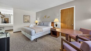 A hotel room with a bed, bedside table, lamp, chair, and a mirror. - Eagle Motel Suite 225 (Manitou Springs)
