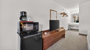 A compact room with a microwave, coffee maker, TV, wooden dresser, and a vanity with a mirror. - Eagle Motel Suite 225 (Manitou Springs)
