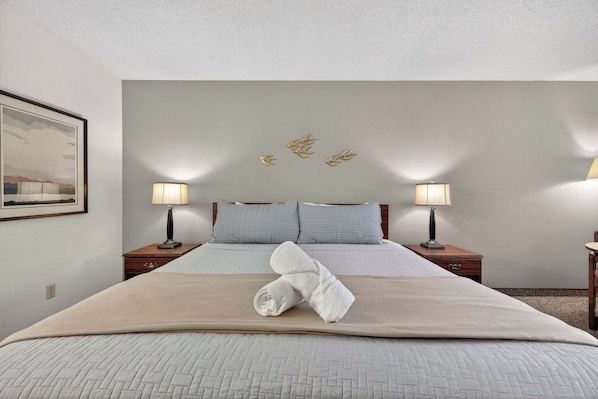 A neatly made bed with a folded towel, two bedside lamps, and a framed picture on the wall.