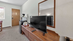 Ein Hotelzimmer mit einem Holztisch, einem Flachbildfernseher, einer Kaffeemaschine, einer Mikrowelle, einer Tür und einem großen Spiegel.
