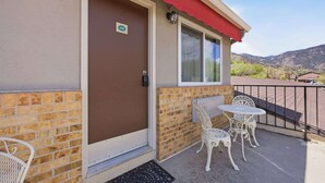 A building with a brown door, a red awning, and a balcony with white metal chairs and a table. - Eagle Motel Suite 226 (Manitou Springs)