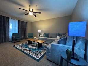 A living room with a ceiling fan, a sofa, a coffee table, a TV, and a patterned rug.