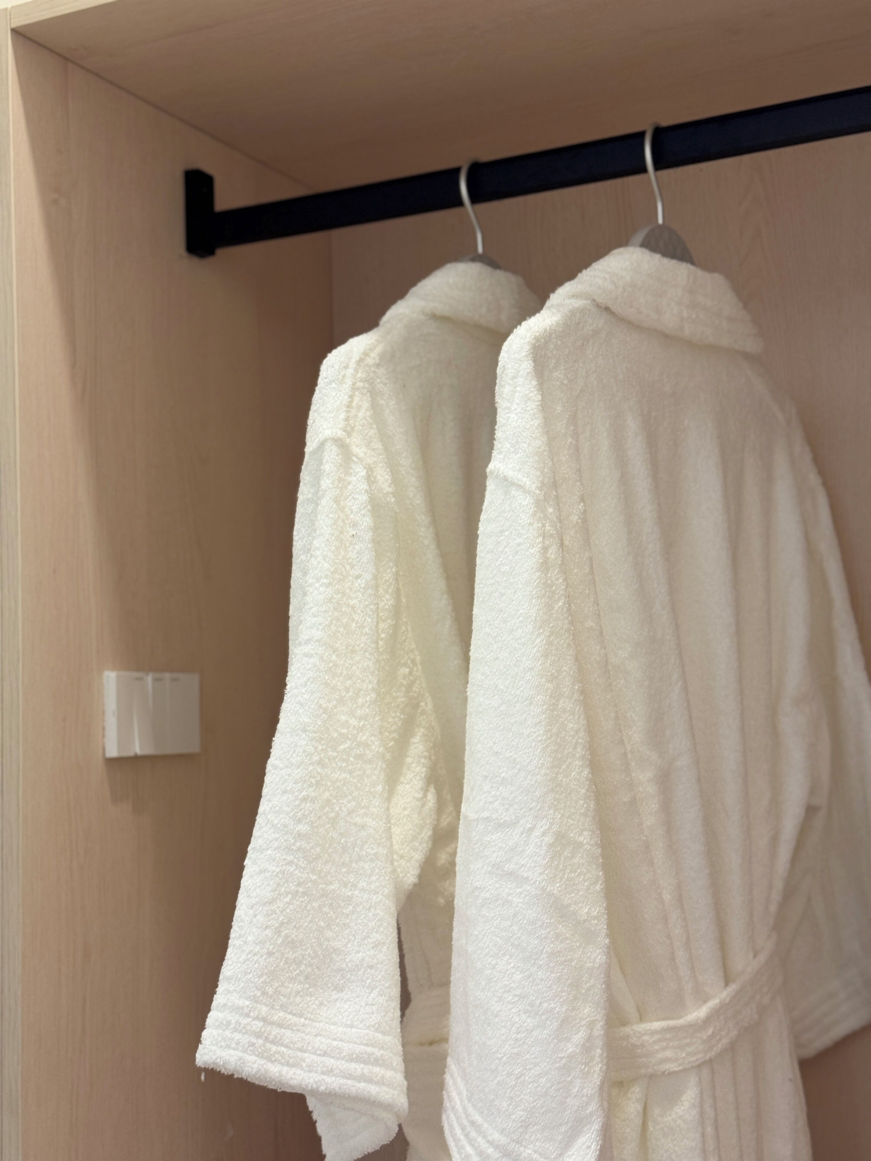 Dos túnicas blancas colgadas de una barra negra en una habitación de madera.