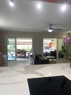 A spacious living area with a sofa, a dining table, and chairs, a ceiling fan, and a view through large sliding doors to an outdoor patio. - Villa near Restaurants, Bars, Beach, Hiking, Pets allowed (Saint-Paul)