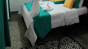 Una habitación con cama, ropa de cama verde y blanca, mosquitera y ventilador.