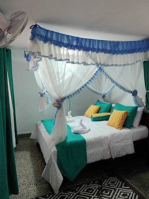 Ein Zimmer mit einem Bett, Bettwäsche in Grün und Weiß, einem Moskitonetz und einem Ventilator.