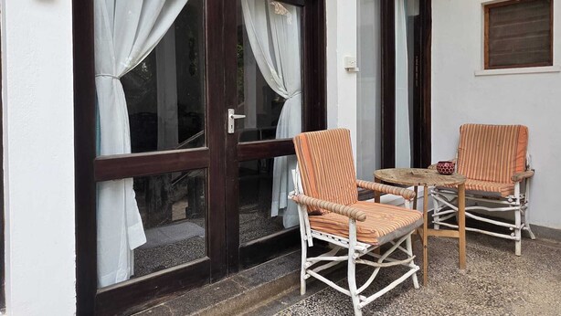 Entrada de una cabaña con un letrero, dos sillones de mimbre y una pequeña mesa.