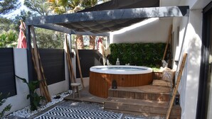 Un bain à remous situé dans un espace extérieur abrité, doté d’une terrasse en bois, et entouré d’un tapis à motifs chevrons noir et blanc.