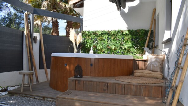 Une terrasse en bois avec un jacuzzi, un petit tabouret et un mur décoratif agrémenté de plantes.
