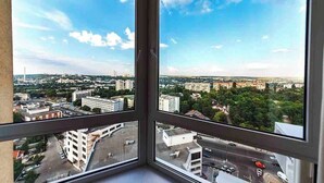 Panoramaudsigt fra et højt vindue over et bybillede med bygninger, veje og grønne områder.