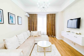A modern living room with a sectional sofa, a round coffee table, a flat-screen TV, and a chandelier. - Park & Lake Skyline 1BD Flat (Chișinău)