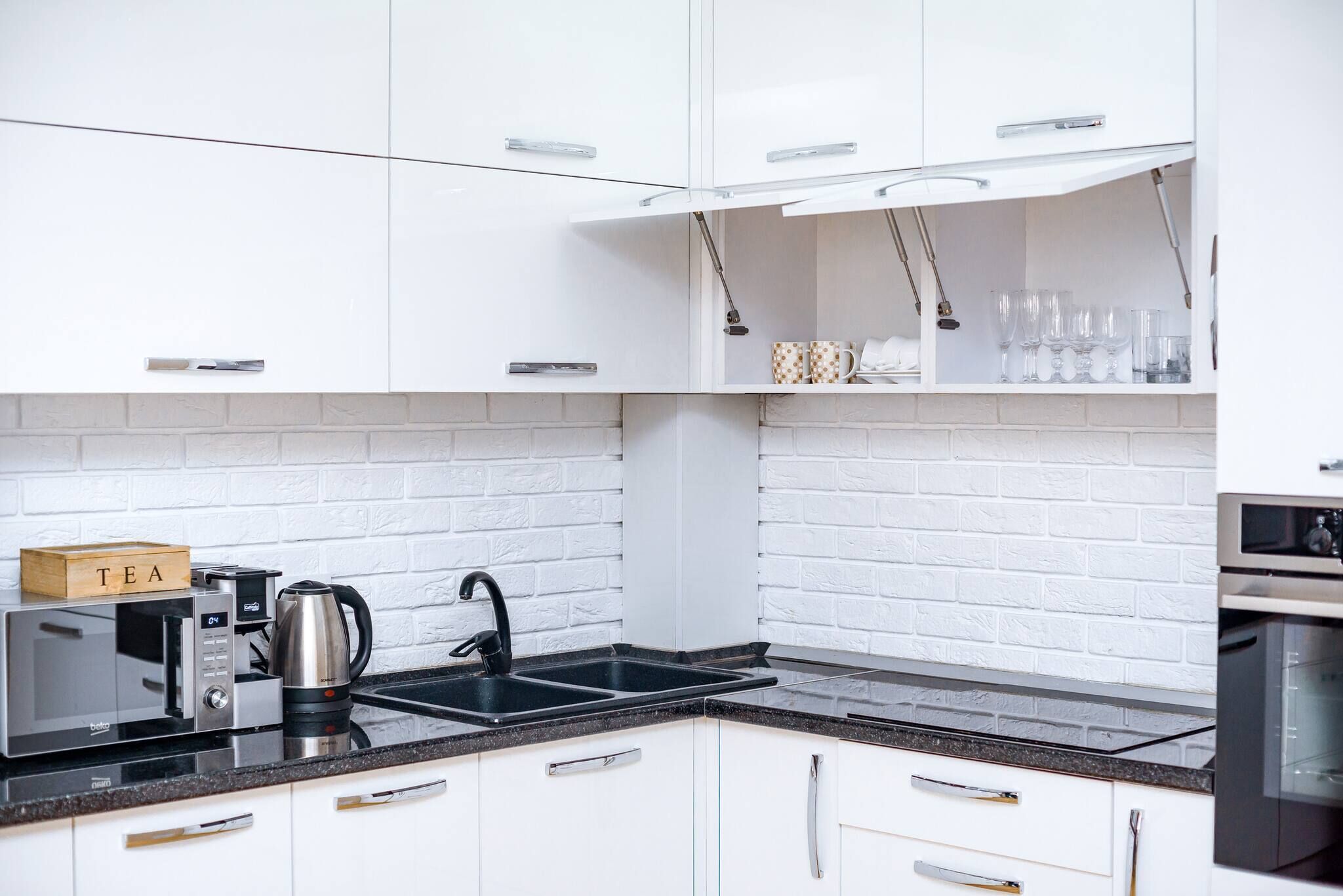 A modern kitchen with white cabinets, a black countertop, a kettle, a microwave, and a coffee maker.