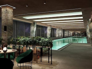 Ett modernt inomhuspoolområde med ett glastak, en sittgrupp med stolar och en skylt med texten ”AQUA TERRA”.