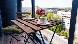 A balcony with a wooden table, two white cups, a glass, and a vase with flowers.