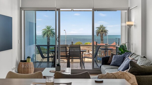 Una sala de estar moderna con un amplio ventanal corredero que da a un balcón con vistas al mar.