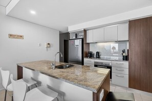 A modern kitchen with a granite countertop, stainless steel appliances, and white cabinetry. - Beach House 305—Oceanfront Balcony Retreat (Victor Harbor)