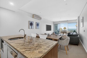A modern kitchen with a granite countertop, a built-in sink, and a dining area with a table and chairs. - Beach House 305—Oceanfront Balcony Retreat (Victor Harbor)