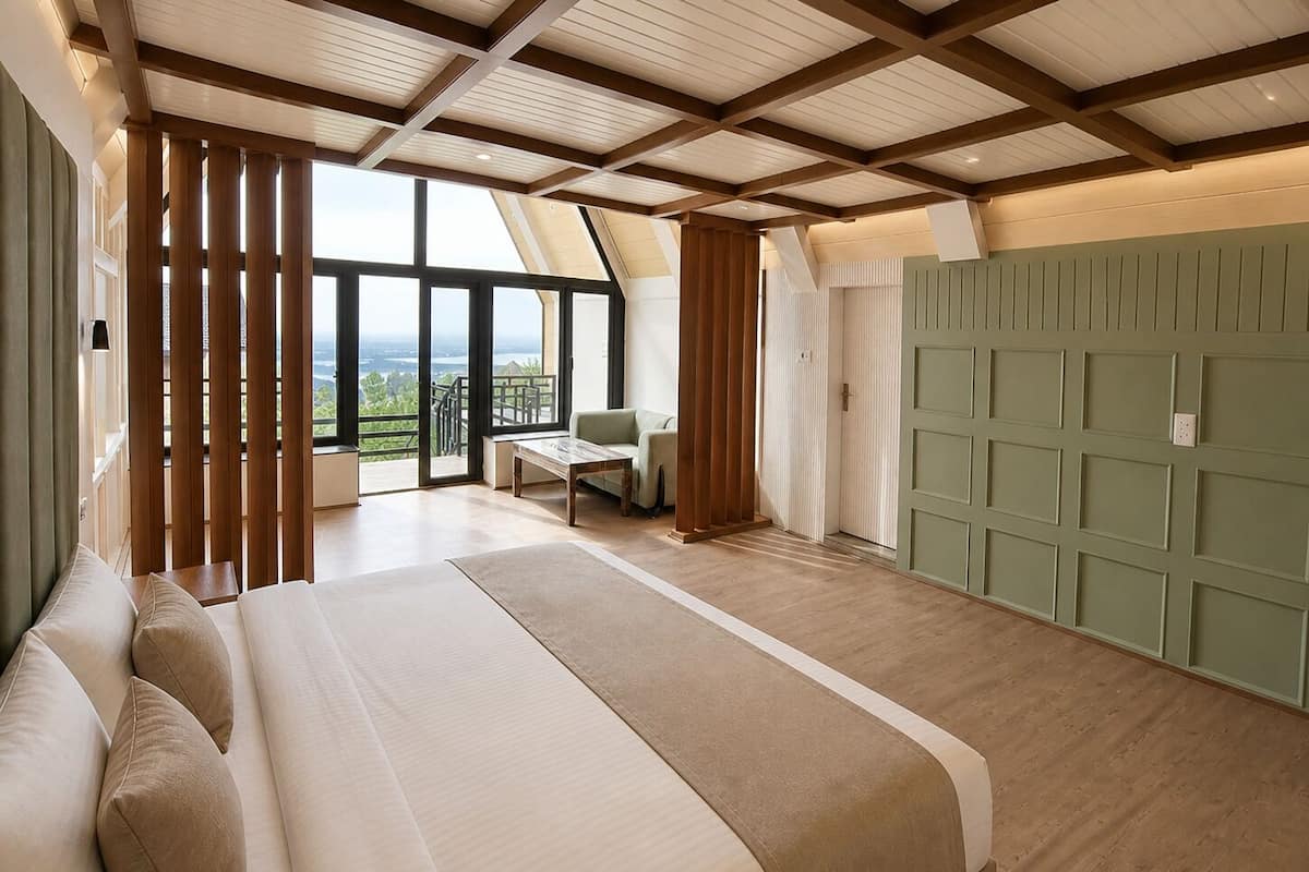 Un dormitorio con una cama grande, vistas por una ventana, un panel de pared verde y una estructura de techo de madera.