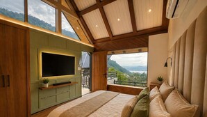 Un dormitorio con una cama grande, un televisor montado en una pared verde y un balcón con vistas a las montañas.