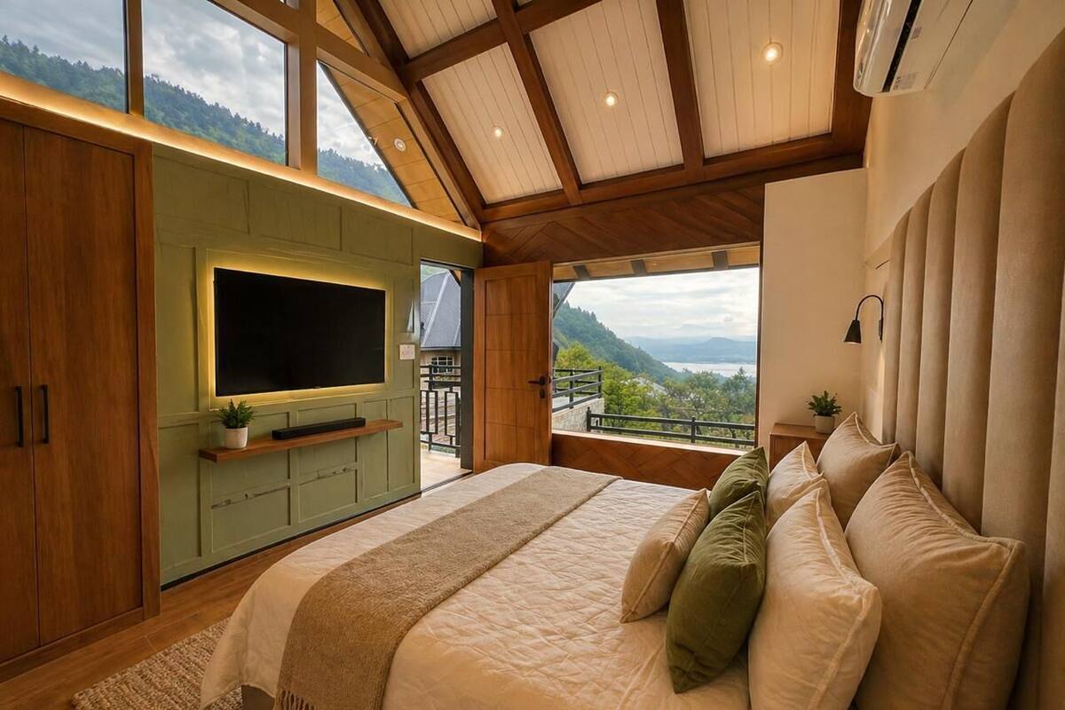 Un dormitorio con una cama grande, un televisor montado en una pared verde y un balcón con vistas a las montañas.