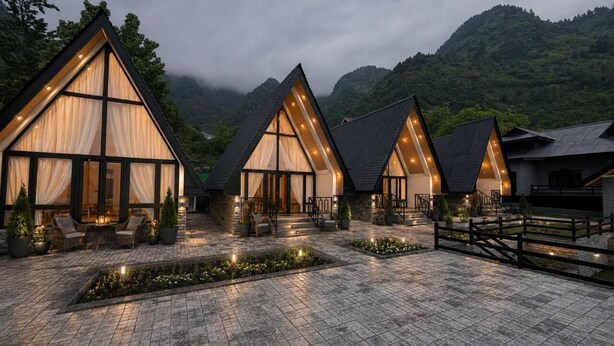 Cabañas modernas de techo triangular, con amplios ventanales, dispuestas en un área pavimentada con plantas en macetas y una valla de madera.