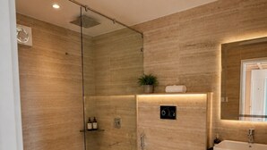 Un baño moderno con ducha envuelta en vidrio, inodoro, lavamanos y espejo.