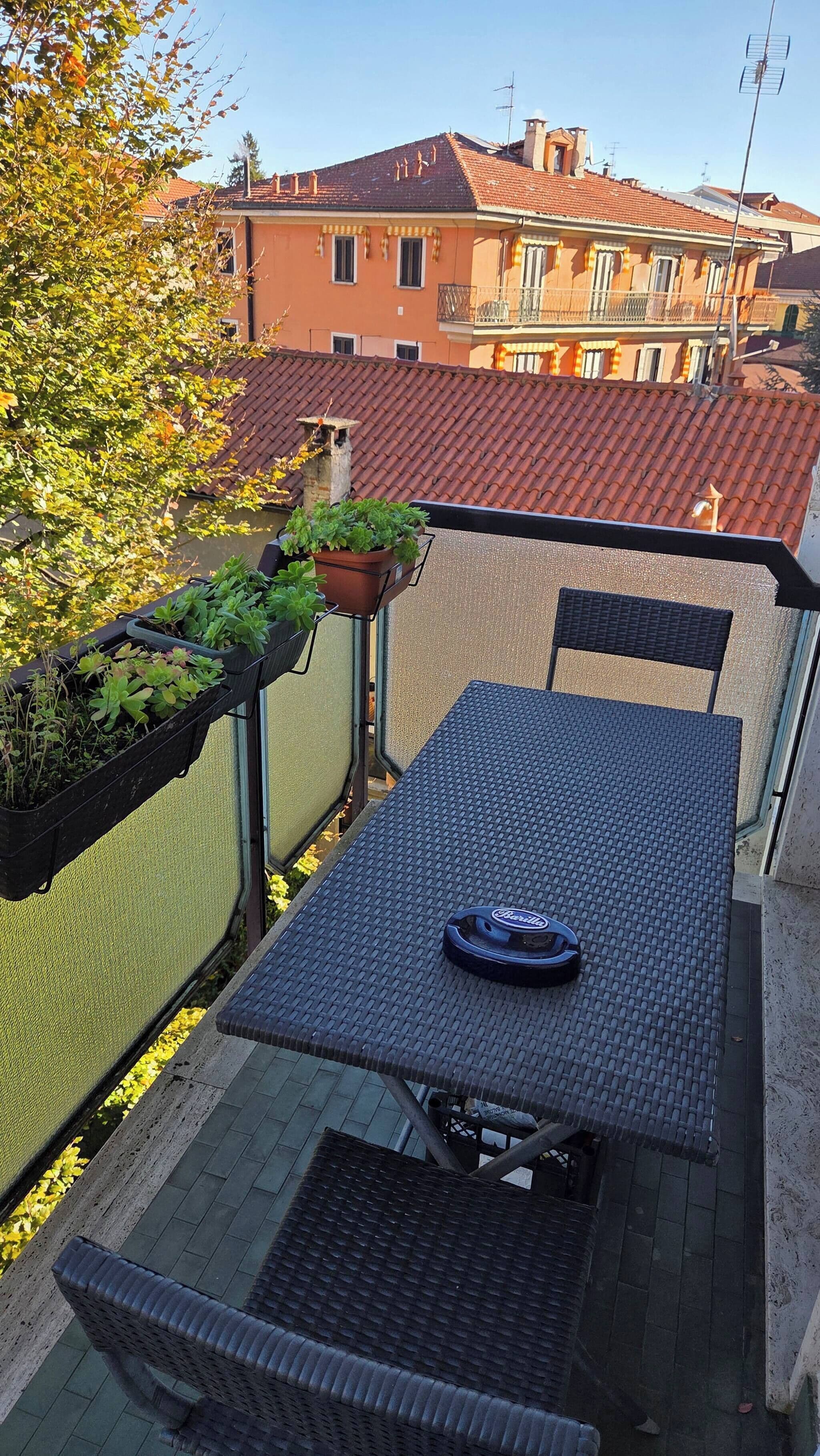 Ein Balkon mit Tisch, Stühlen, einem Blumentopf und Blick auf Gebäude.