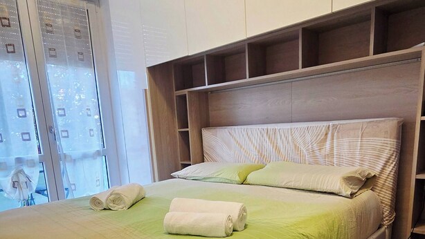 A modern bedroom with a large bed, built-in storage, and a view of the city. - Charming Central Apartment Near Lake Maggiore in Arona (Arona)