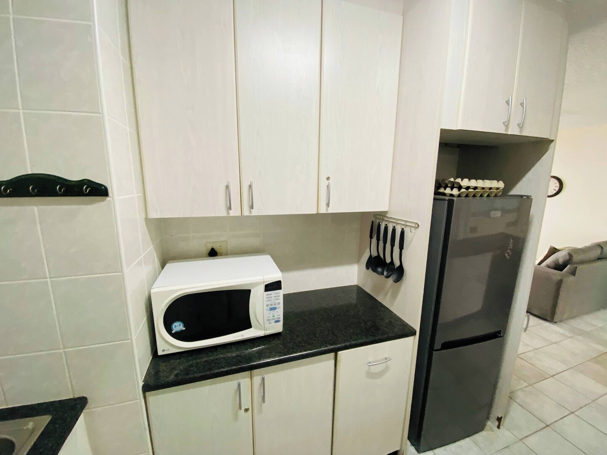 A kitchen with white cabinets, a black countertop, a white microwave, and a black refrigerator.