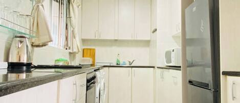A kitchen with white cabinets, a stainless steel refrigerator, a microwave, and a kettle on the counter.