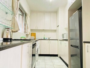 Eine Küche mit weißen Schränken, einem Edelstahl-Kühlschrank, einer Mikrowelle und einem Wasserkocher auf der Arbeitsplatte.