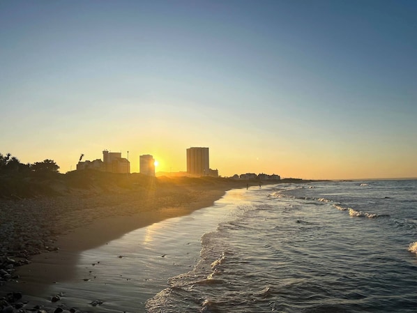A beach with a sunset, buildings in the background, and waves.