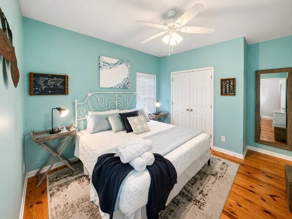 Une chambre à coucher comprenant un lit, un bureau, une chaise, un ventilateur de plafond et une porte.
