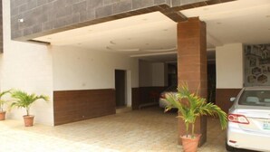 A building entrance with a tiled patio, a parked car, and potted plants. - De Grandeur Tower Apartment (Ojodu)
