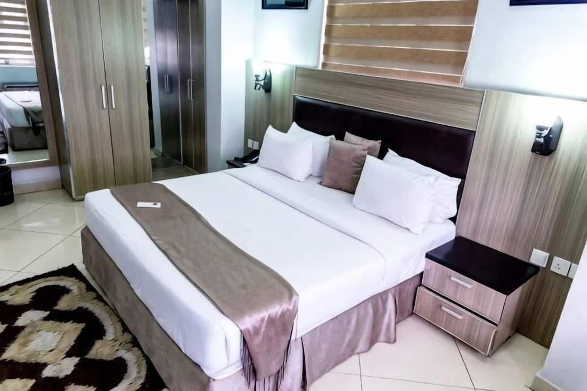 A neatly made bed with a white and brown bedspread, a bedside table with a lamp, and a wardrobe with a mirror.