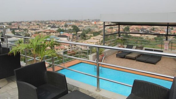 A rooftop pool with lounge chairs, a view of a residential area, and a clear sky. - De Grandeur Tower Apartment (Ojodu)