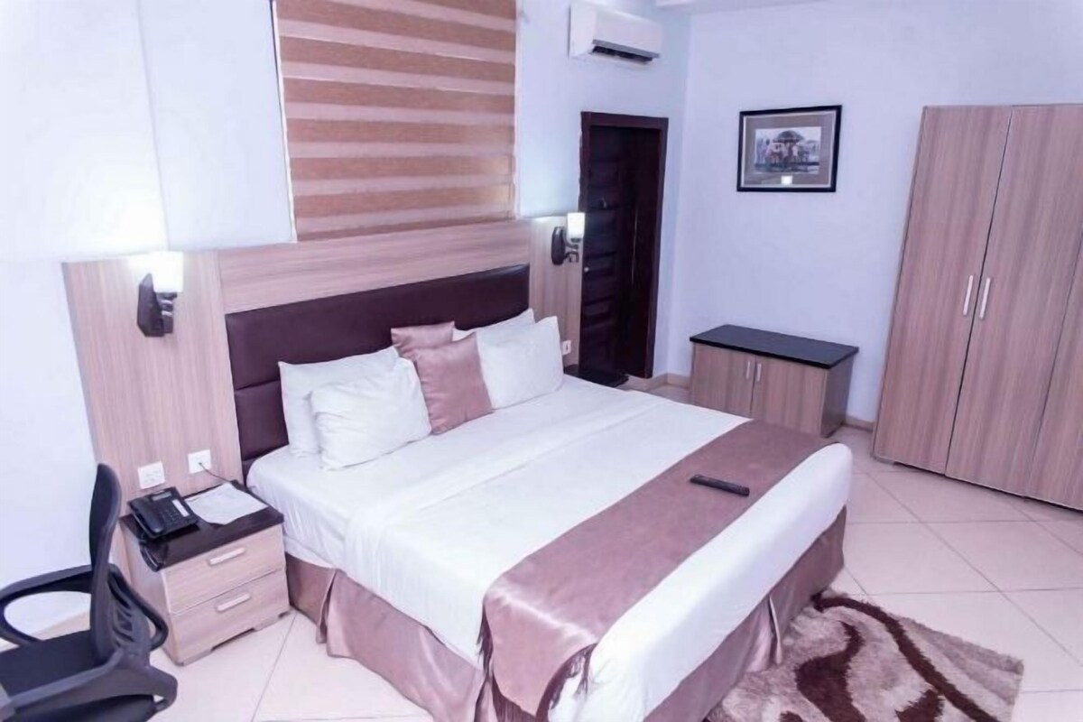 A bedroom with a bed, bedside table, chair, wardrobe, and a framed picture on the wall.