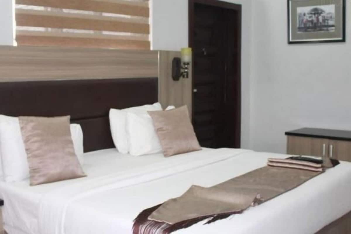 A neatly made bed with a white comforter and multiple pillows, a bedside table with a lamp, and a framed picture on the wall.