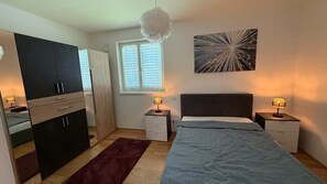 A bedroom with a bed, bedside tables, a wardrobe, a window, and a wall-mounted artwork. - Fantastic garden apartment, close to the center and close to Salzburg (Freilassing)