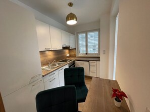 A modern kitchen with white cabinets, a wooden countertop, a sink, and a window with blinds. There is a dining table with chairs and a potted plant. - Fantastic garden apartment, close to the center and close to Salzburg (Freilassing)