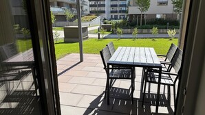 A patio with a table and chairs, a view of a building complex, and a grassy area.