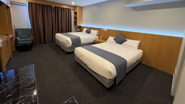 A hotel room with two beds, a chair, a desk, and a wardrobe.