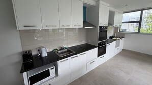 A modern kitchen with white cabinets, a black countertop, a built-in oven, and a window providing a view of the outside.