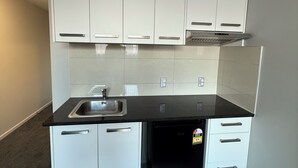 A compact kitchen with white cabinets, a black countertop, a built-in dishwasher, and a Panasonic air conditioner.