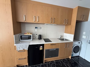 A compact kitchen with wooden cabinets, a microwave, a coffee maker, a dishwasher, and a washing machine. - Goodview Hotel (Auckland)
