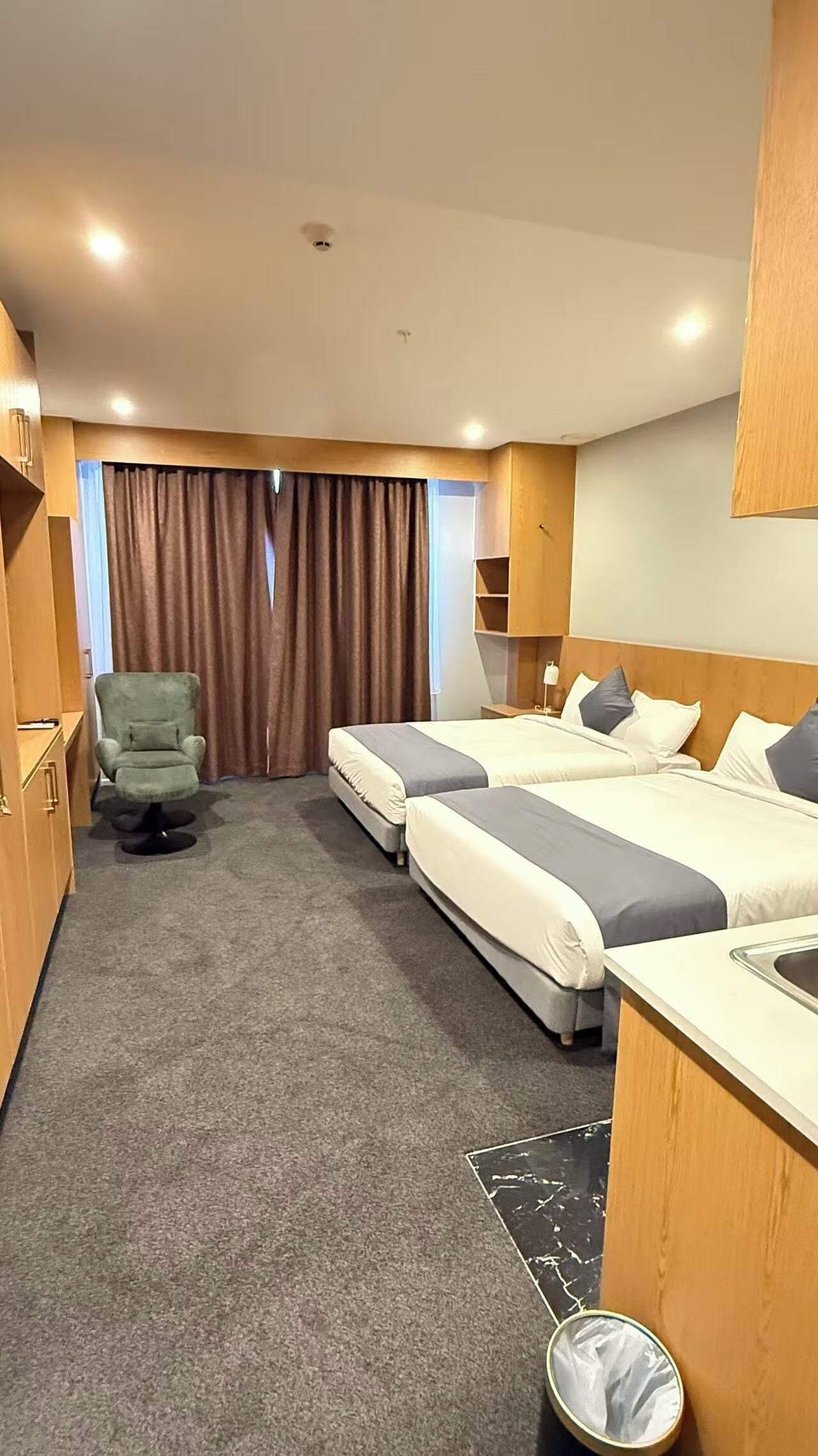 Ein Hotelzimmer mit zwei Betten, einem Schreibtisch, einem Stuhl und einer kleinen Küchenzeile.