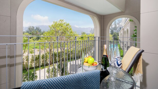 Un balcone con vista su una piscina, una ciotola di frutta, una bottiglia di champagne e un bicchiere.