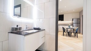 Un bagno moderno con uno specchio grande, un lavandino e un water. Si vede attraverso una porta aperta anche un'area pranzo con tavolo e sedie.